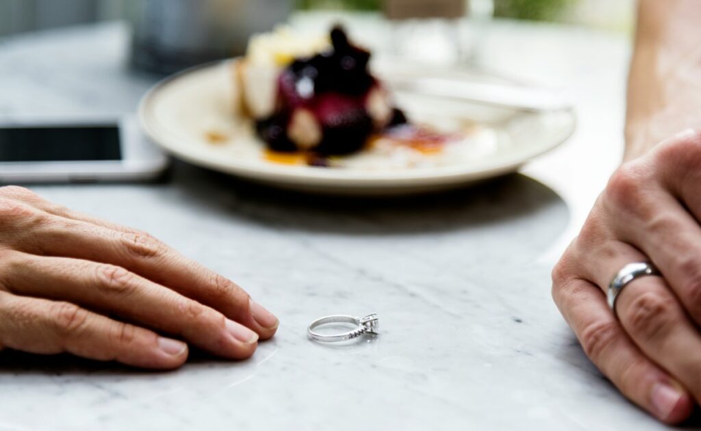 A quiet, reflective moment between two people as a wedding ring rests on the table—symbolising a relationship transitioning with calm, respect, and mutual understanding.